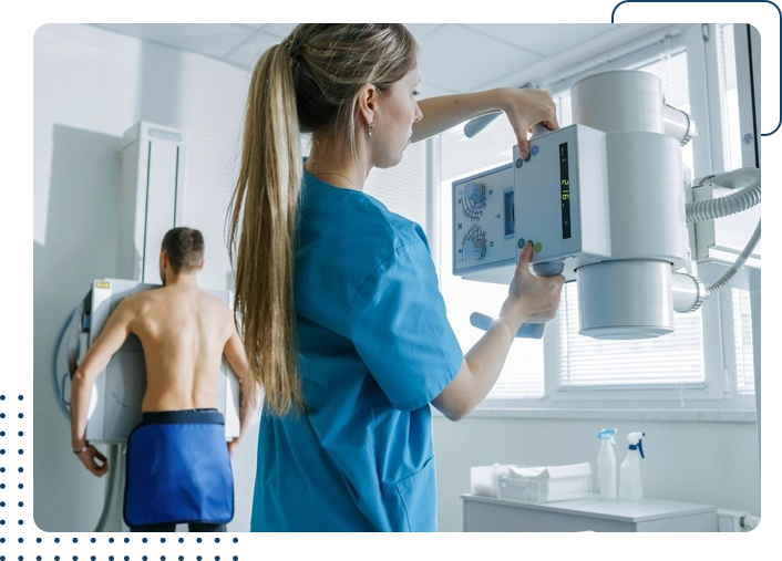 A woman in blue scrubs is holding an x-ray machine.